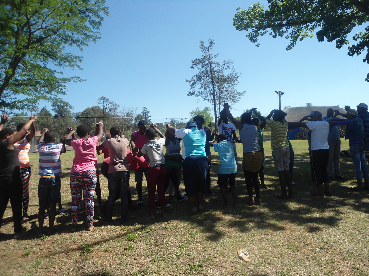Children and youth standing in a circle during a Siyakhana outdoor programme